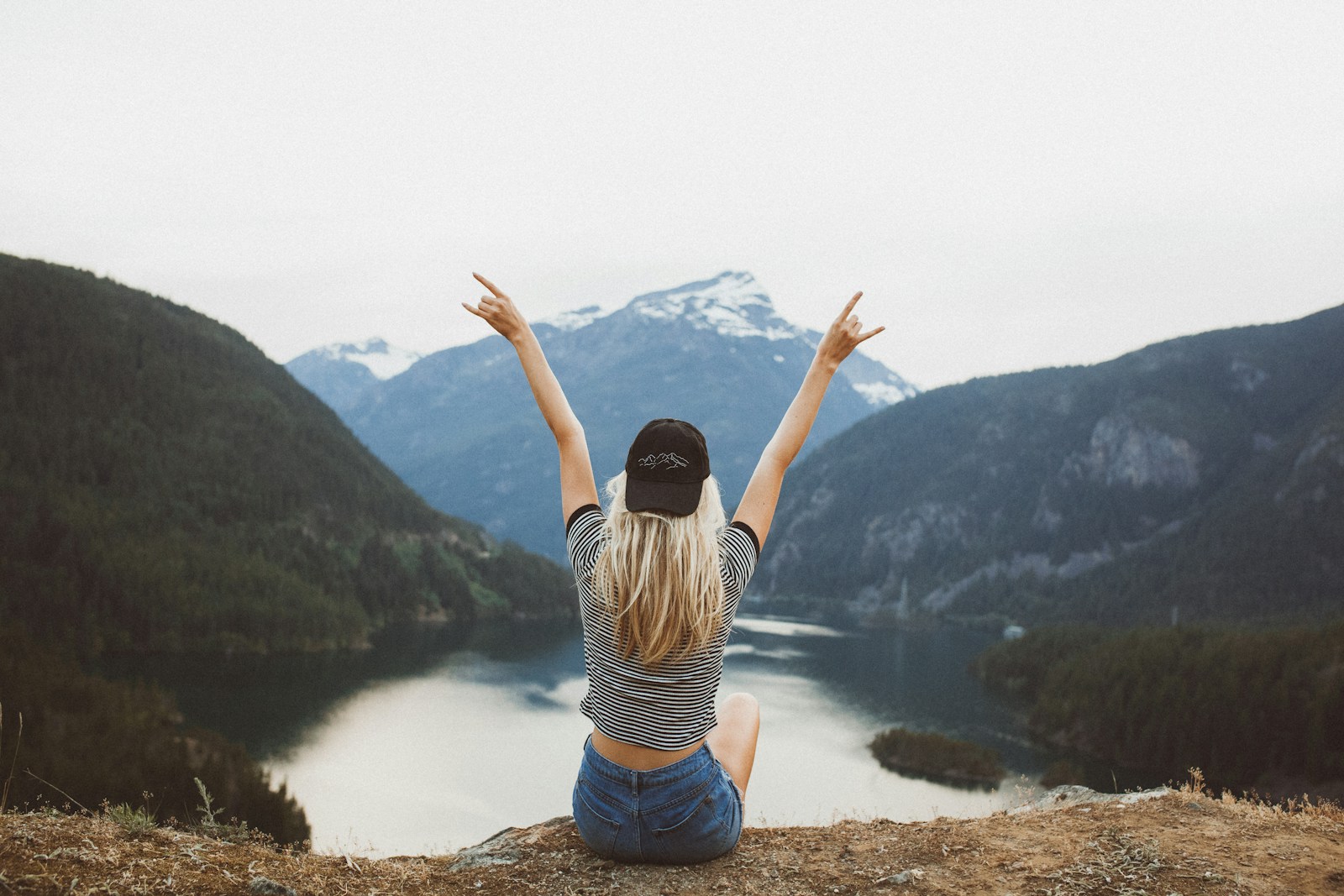 woman sitting on cliff raising both hands Open Your Heart